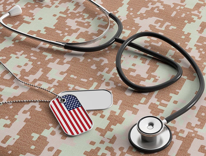 Dog Tags, one with an American Flag laying with a stethoscope on camouflage