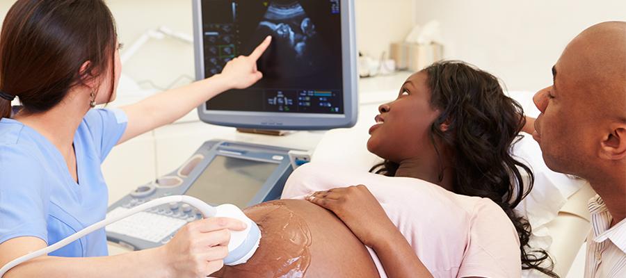 Designing Efforts to Improve Black Maternal Health. An ultrasound technician performs an ultrasound and shares an ultrasound image with a black couple of their unborn child..